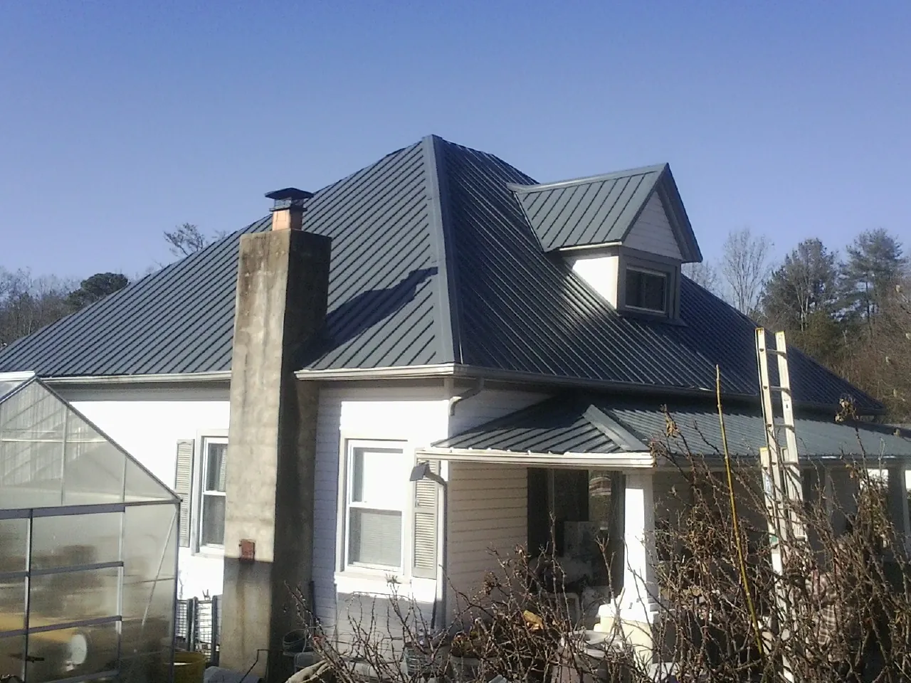 Dark blue standing seam metal roof on a white farmhouse with dormer — Slate & Tile Roof Repair by Roofing Brothers in Cabins