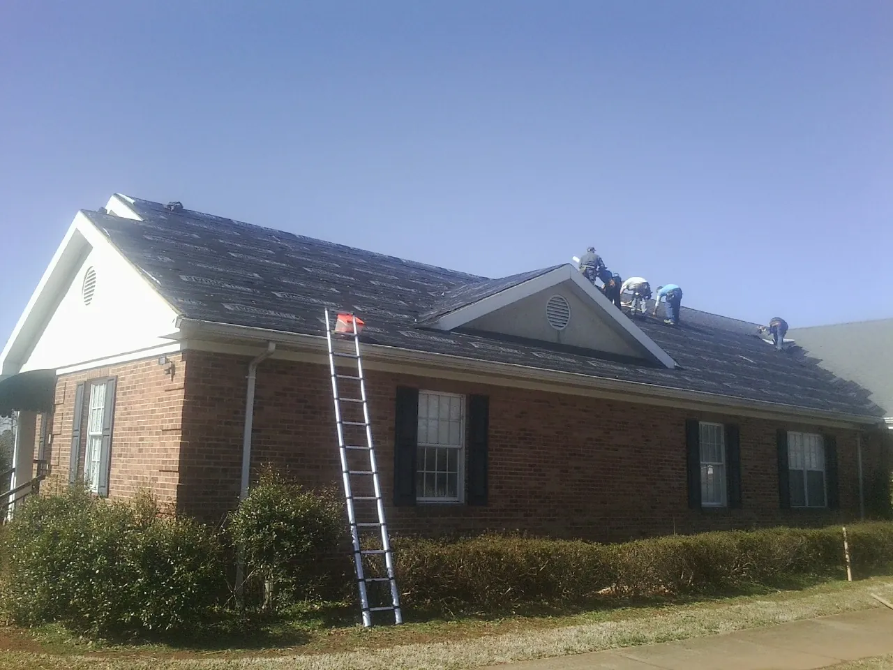 Crew tearing shingles off a brick ranch roof with a ladder set — Metal Roof Repair work by our crew in Cabins