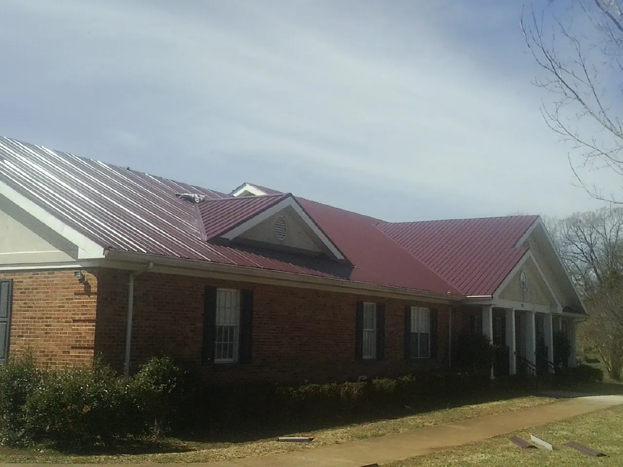 Red metal roof with gabled entries on a long brick building, from a Hail Damage Roof Repair job in Cabins