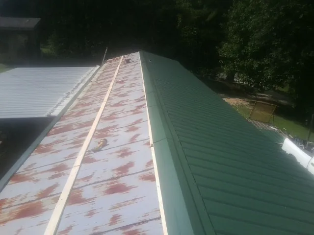 Old rusted panels beside newly installed green metal roofing — Wind Damage Roof Repair by Roofing Brothers in Cabins
