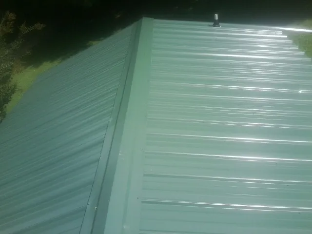 New green metal panels meeting at the ridge of a roof — Flat Roof Repair work by our crew in Cabins