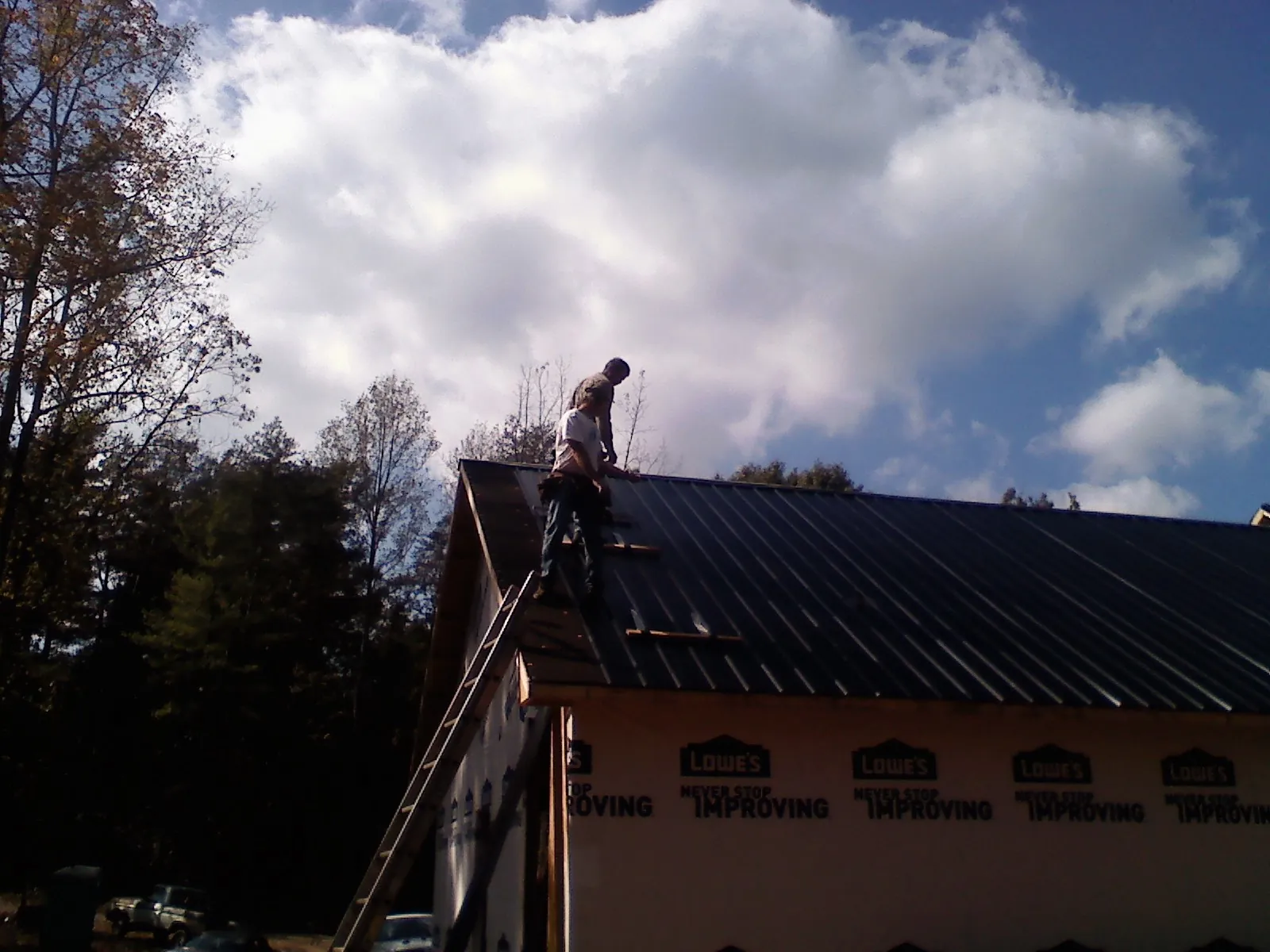 Roofer fastening dark metal panels high against a cloudy sky, from a Roof Inspection job in Cabins
