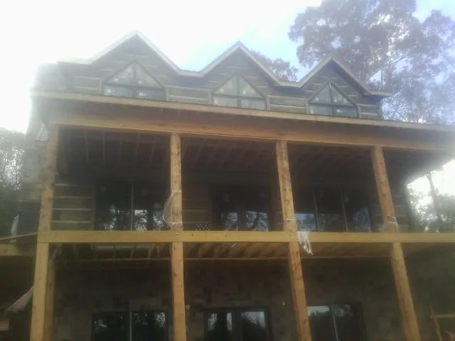 Dormers and porch framing on a large log home under construction — Roof Coating work by our crew in Cabins