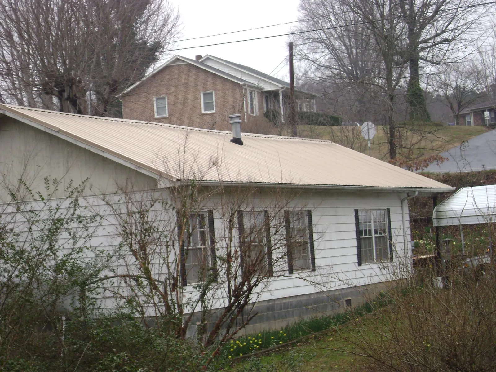 Tan metal roof on a white sided house set into a hillside — Commercial Roofing by Roofing Brothers in Cabins