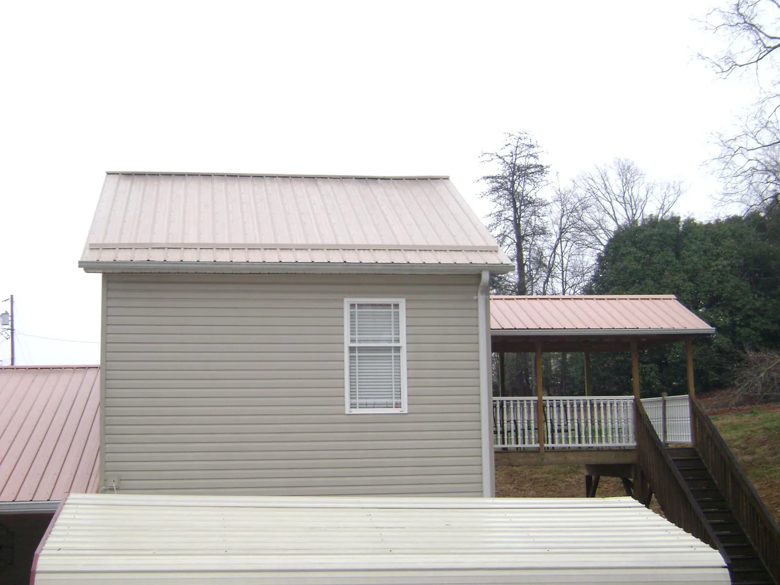 Tan metal roofs on a two story addition and attached porch, from a Roof Replacement job in Cabins